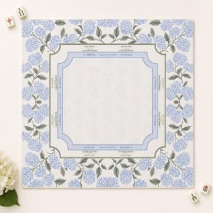 May include: A square Mahjong mat featuring a white centre with light blue border markings and text including Charleston 1, Charleston 2, Walls Left, and Play Right. The border is decorated with a repeating pattern of light blue hydrangea flowers.