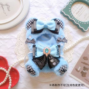 May include: A light blue pet outfit with black and white checkered accents and bows. The outfit features a large bow with a jewel in the center and smaller bows on the ears and sleeves. The outfit is designed to resemble a teddy bear.