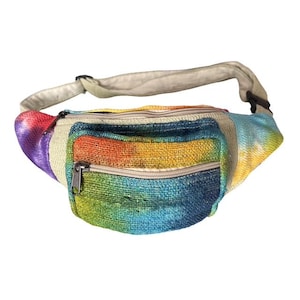 Pode incluir: Uma pochete feita de tecido texturizado com um padrão tie-dye vibrante em tons de roxo, laranja, amarelo, verde e azul. A bolsa inclui um compartimento principal com zíper e um bolso frontal menor com zíper, acompanhada por uma alça bege.
