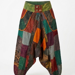 Op de afbeelding: Patchwork harembroek met een hoge groene tailleband en vier ronde knopen. De broek is opgebouwd uit diverse stoffen vierkanten in tinten rood, oranje, groen, paars en donkergrijs, inclusief een gedeelte met een patroon van zwarte cirkels.