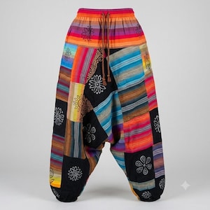Op de afbeelding: Harembroek met een patchworkontwerp met horizontale strepen in oranje, roze, paars en blauw, afgewisseld met effen zwarte panelen. De zwarte delen zijn versierd met witte bloemen- en paisleyprints en de taille is voorzien van een trekkoord.