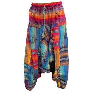 Peut inclure: Pantalon sarouel ample présentant un motif patchwork vibrant avec des rayures horizontales et verticales dans des tons orange, rouge, violet, bleu et jaune. Le tissu est orné de motifs noirs de soleils et de fleurs avec une taille à cordon.