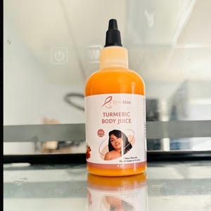 Op de afbeelding: Een oranje vloeistof in een doorzichtige plastic fles met een zwarte, puntige applicator dop. Het witte etiket bevat de tekst Turmeric Body Juice, een afbeelding van een persoon en het volume van 118 ml. De fles is cilindervormig.