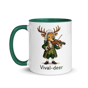 May include: A white ceramic mug with a dark green handle and rim, featuring a cartoon deer dressed in an 18th-century green coat and white wig, playing a violin. Below the illustration, the text Vival-deer is printed in black and green.