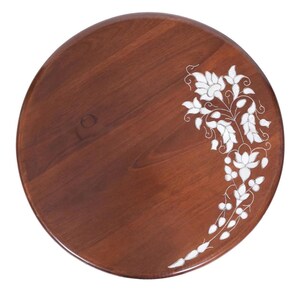 K&ouml;nnte beinhalten: Ein rundes Holztablett mit einem satten braunen Finish, das ein kompliziertes wei&szlig;es Blumen-Intarsien-Design aufweist, das sich entlang der rechten Seite kr&uuml;mmt. Die Holzmaserung ist auf der glatten Oberfl&auml;che sichtbar und bildet einen Kontrast.