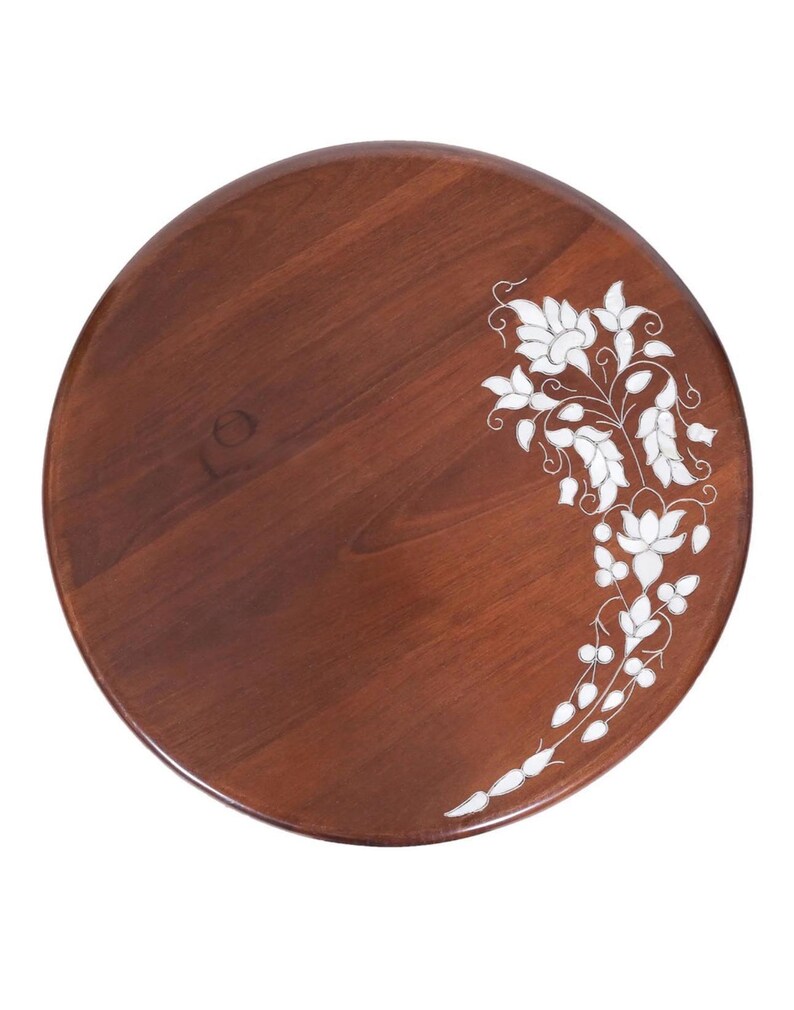 K&ouml;nnte beinhalten: Ein rundes Holztablett mit einem satten braunen Finish, das ein kompliziertes wei&szlig;es Blumen-Intarsien-Design aufweist, das sich entlang der rechten Seite kr&uuml;mmt. Die Holzmaserung ist auf der glatten Oberfl&auml;che sichtbar und bildet einen Kontrast.
