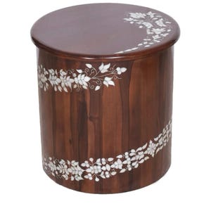 K&ouml;nnte beinhalten: Ein zylindrischer Beistelltisch aus Holz mit einer glatten, dunkelbraunen Oberfl&auml;che. Das M&ouml;belst&uuml;ck ist mit einem eingelegten wei&szlig;en Blumenrankenmuster verziert, das sich um die Seite windet und &uuml;ber den oberen Rand erstreckt.