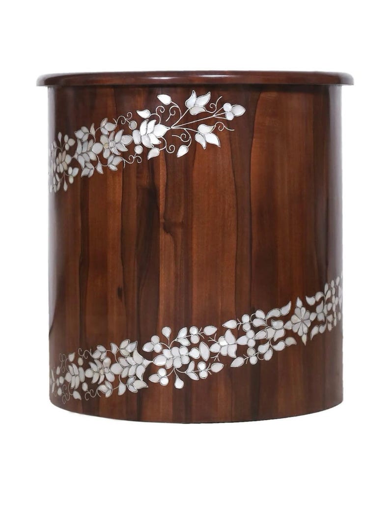 K&ouml;nnte beinhalten: Ein zylindrischer Beistelltisch aus Holz mit einer glatten, dunkelbraunen Oberfl&auml;che. Das &Auml;u&szlig;ere ist mit zwei diagonalen B&auml;ndern aus wei&szlig;er Blumenintarsie verziert, die komplizierte Blatt- und Blumenmuster auf der gew&ouml;lbten Fl&auml;che zeigen.