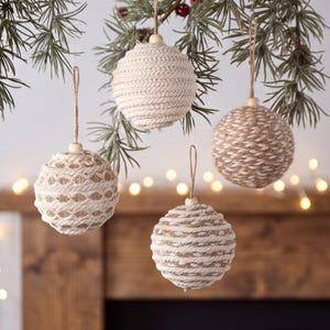 May include: Four spherical Christmas ornaments hanging from a pine branch. Each ornament is wrapped in a combination of natural tan jute twine and white cotton cord, featuring a small wooden bead at the top and a thin brown hanging string.