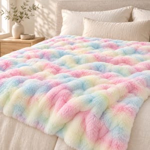 Może przedstawiać: Pluszowy koc ze sztucznego futra z miękkim, wielokolorowym pastelowym wzorem tie-dye w odcieniach różu, błękitu, żółci i bieli. Koc ma grubą, kudłatą fakturę i jest narzucony na łóżko z pościelą w neutralnych kolorach.