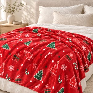 Könnte beinhalten: Eine leuchtend rote Plüschdecke mit einem wiederkehrenden Weihnachtsmuster aus grünen Tannenbäumen, weißen Schneeflocken, rot-grünen Geschenkkartons und Zuckerstangen, die in einem festlichen Design über die gesamte Stoffoberfläche verteilt sind.
