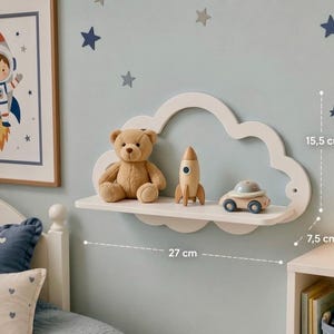 May include: A white cloud-shaped wall shelf measuring 27 cm in width, 15.5 cm in height, and 7.5 cm in depth. The shelf holds a tan teddy bear, a wooden rocket ship toy, and a small wooden toy car with a grey top and blue wheels.