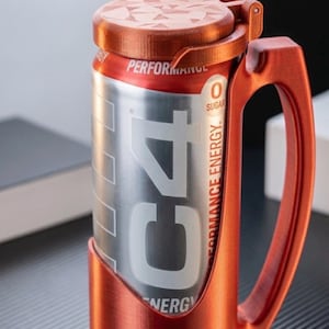 May include: A metallic copper-coloured plastic holder with a handle and a hinged lid, designed to fit a silver C4 energy drink can. The holder features a textured finish and securely encases the lower portion of the can while the lid covers the top.