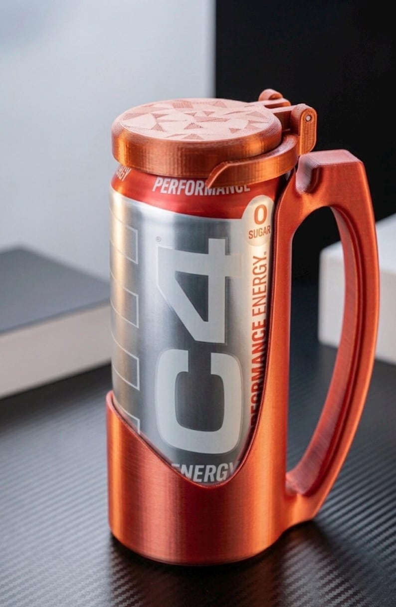 May include: A metallic copper-coloured plastic holder with a handle and a hinged lid, designed to fit a silver C4 energy drink can. The holder features a textured finish and securely encases the lower portion of the can while the lid covers the top.