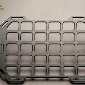 Könnte beinhalten: Eine rechteckige schwarze Metallplatte mit einem Gitter aus fünfundzwanzig gleichmäßigen quadratischen Ausschnitten. Der Rahmen verfügt über abgerundete Ecken mit integrierten Schlitzen und kleinen kreisförmigen Montagelöchern an den Kanten.