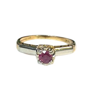 May include: A gold ring with a small, round, red gemstone set in a square setting. The band is a simple, classic design, perfect for everyday wear. The ring is set against a white background.