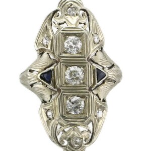 Pu&ograve; includere: Un anello vintage con un design a filigrana che presenta un gruppo centrale di diamanti e due pietre di zaffiro pi&ugrave; piccole.