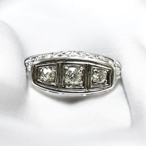 May include: A silver ring with three square-shaped diamonds set in a decorative band.