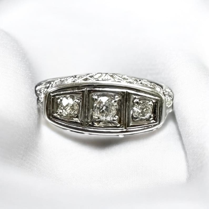 May include: A silver ring with three square-shaped diamonds set in a decorative band.
