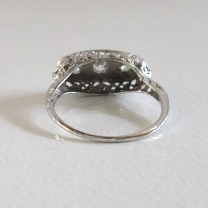 May include: A silver ring with a delicate filigree design and three round gemstones set in the center.