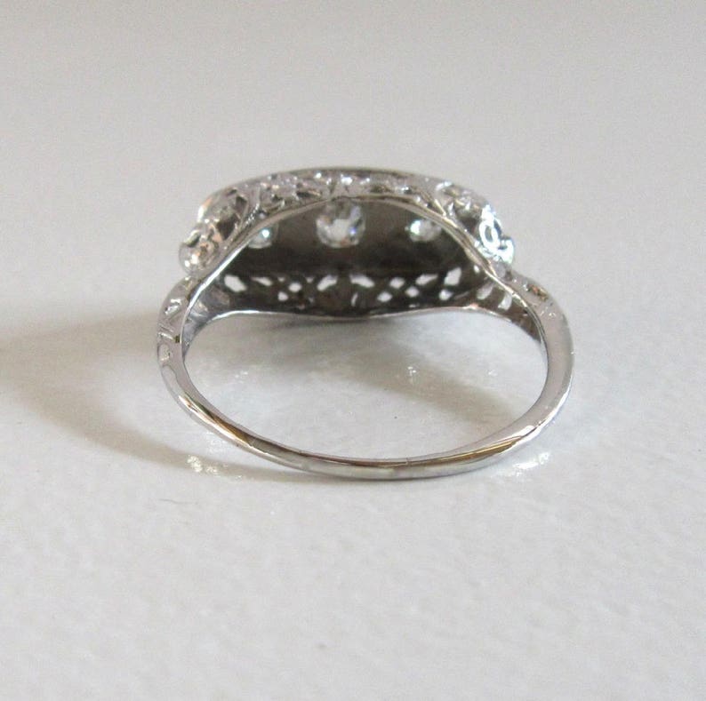 May include: A silver ring with a delicate filigree design and three round gemstones set in the center.