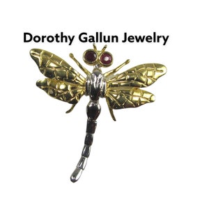 May include: Gold and silver dragonfly brooch with red gemstone eyes. Dorothy Gallun Jewelry.
