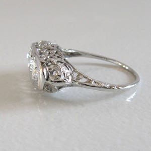 May include: A silver filigree ring with a square-shaped center stone and two smaller stones on either side.