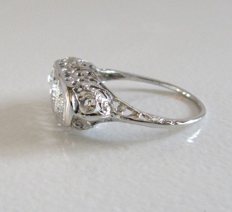 May include: A silver filigree ring with a square-shaped center stone and two smaller stones on either side.