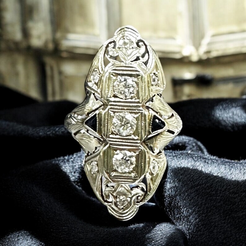 Pu&ograve; includere: Un anello d'argento con un design geometrico che presenta cinque diamanti rotondi disposti in fila. L'anello ha un design delicato e intricato con un'estetica vintage.