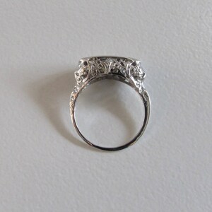 May include: A silver filigree ring with a rectangular center stone setting. The ring is detailed with floral designs and has a delicate, vintage aesthetic.