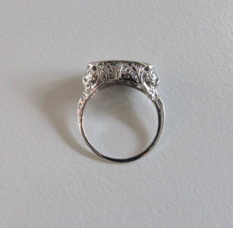 May include: A silver filigree ring with a rectangular center stone setting. The ring is detailed with floral designs and has a delicate, vintage aesthetic.