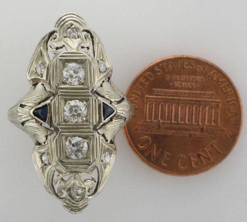 Pu&ograve; includere: Un anello d'argento vintage con un design geometrico che presenta un gruppo centrale di diamanti e diamanti pi&ugrave; piccoli che circondano il centro. L'anello ha anche quattro piccoli zaffiri blu.