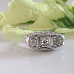 May include: A silver ring with three square-shaped diamonds set in a decorative band.
