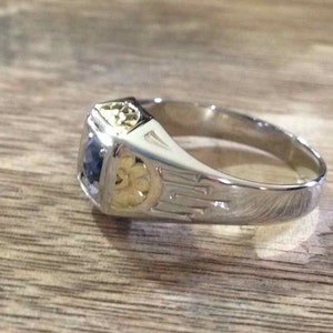 May include: A silver ring with a blue gemstone and gold accents. The ring has a detailed design with intricate patterns.