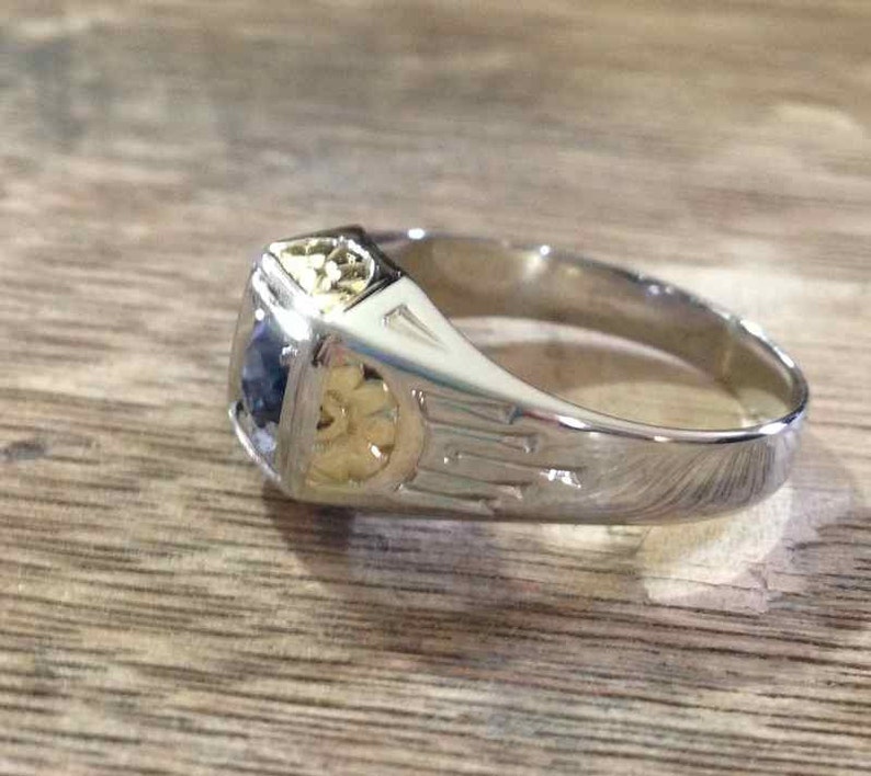 May include: A silver ring with a blue gemstone and gold accents. The ring has a detailed design with intricate patterns.