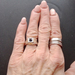 May include: A hand wearing a silver ring with a black stone and a set of three silver bands on the ring finger.