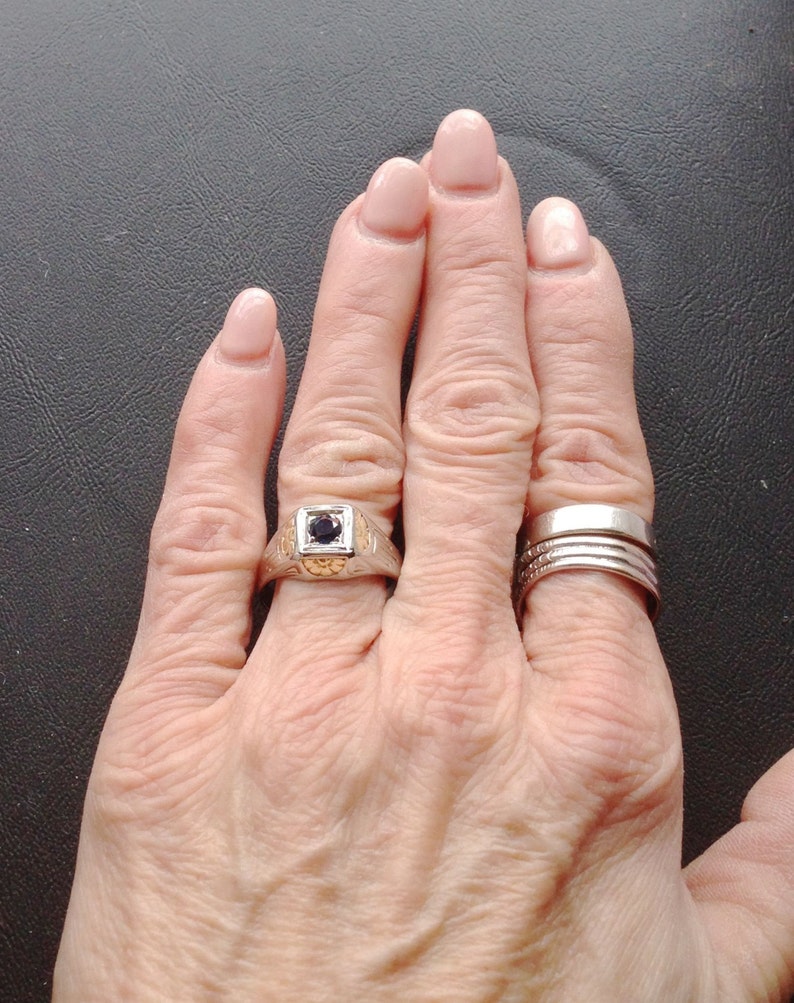 May include: A hand wearing a silver ring with a black stone and a set of three silver bands on the ring finger.