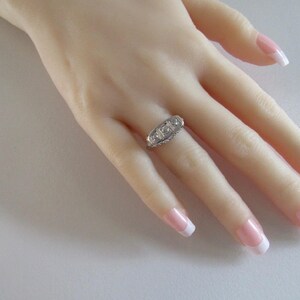 May include: A silver ring with three clear gemstones set in a row. The ring is on a model's finger.
