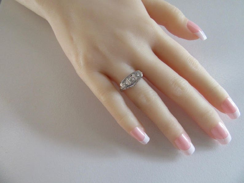 May include: A silver ring with three clear gemstones set in a row. The ring is on a model's finger.
