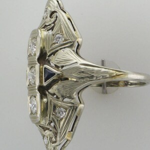 Pu&ograve; includere: Un anello vintage in argento con uno zaffiro blu e diamanti incastonati in un intricato design Art Deco.