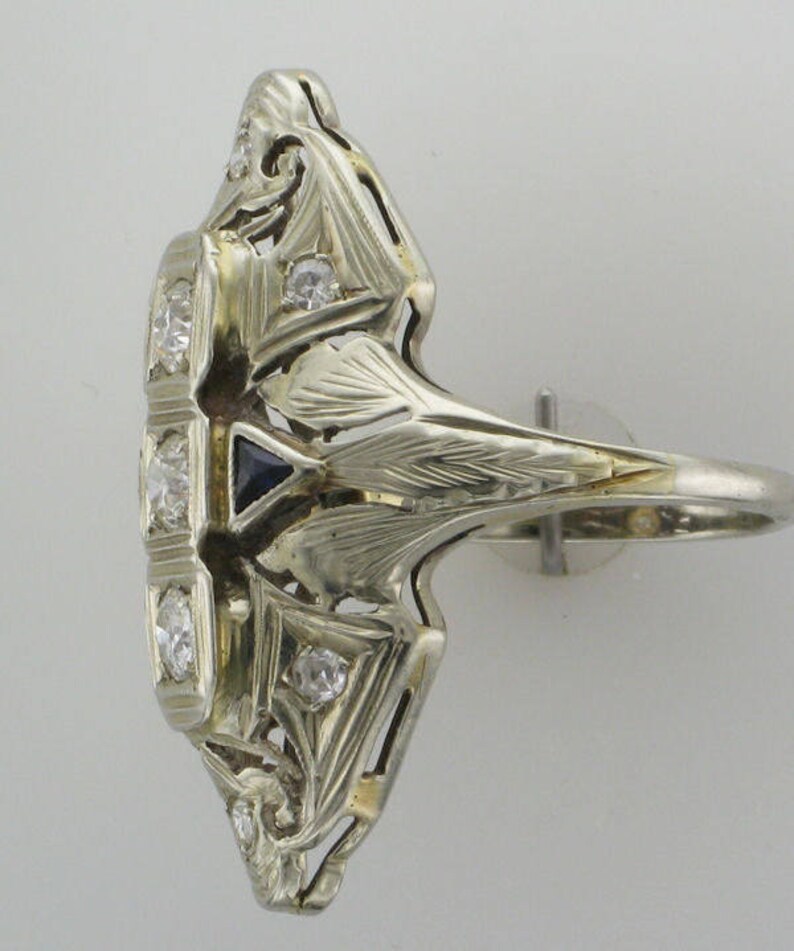 Pu&ograve; includere: Un anello vintage in argento con uno zaffiro blu e diamanti incastonati in un intricato design Art Deco.