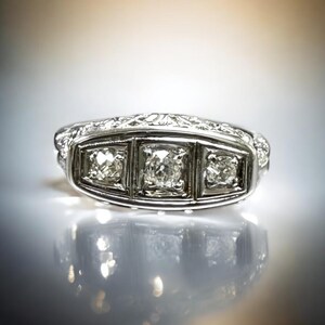 May include: A silver ring with three square-shaped diamonds set in a decorative band.