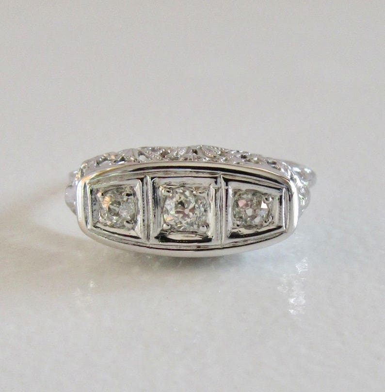 May include: A silver ring with three round diamonds set in a delicate filigree design.