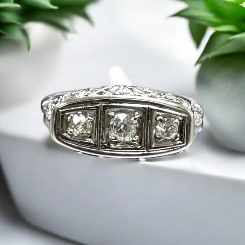 May include: A silver ring with three square-shaped diamonds set in a decorative band.