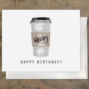 May include: A white coffee cup with a brown paper sleeve that says "Wesley" on it. The text "Happy Birthday!" is below the cup.