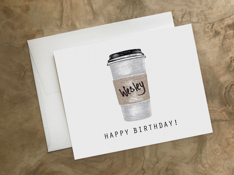 May include: A white card with a black and white illustration of a coffee cup with a brown paper sleeve that says "Wesley" on it. The text "Happy Birthday!" is printed below the cup.