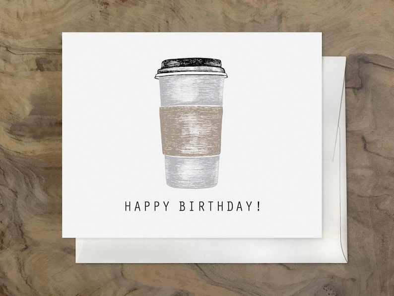 May include: A white and gray coffee cup with a brown paper sleeve and a black lid. The text "HAPPY BIRTHDAY!" is printed below the cup.