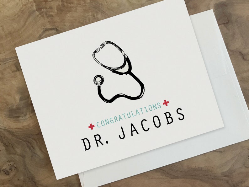 May include: A white card with a black and white illustration of a stethoscope. The card has the text "Congratulations + Dr. Jacobs" in black and red.