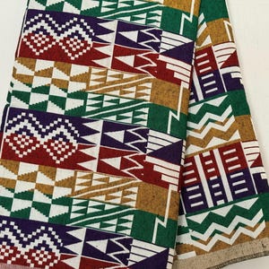 May include: A folded piece of fabric featuring a repeating geometric pattern in vibrant shades of red, green, purple, and gold on a white background. The design consists of alternating horizontal bands of zigzags, triangles, and checkered squares.