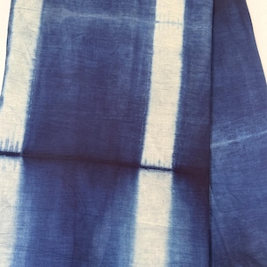 May include: A piece of fabric featuring a tie-dye pattern with deep indigo blue and off-white vertical stripes. The design displays a gradient effect where the blue colour transitions into the white sections, creating a soft, blurred edge between the colours.
